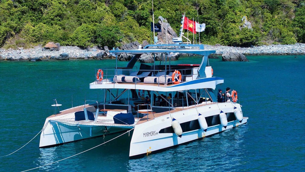 A large, multi-deck boat named 'MARMORIS99' anchored near a rocky shore with lush greenery in the background. 4