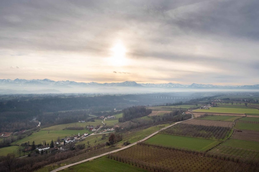 A rural landscape with fields, a small village, and distant mountains under a cloudy sky. 2