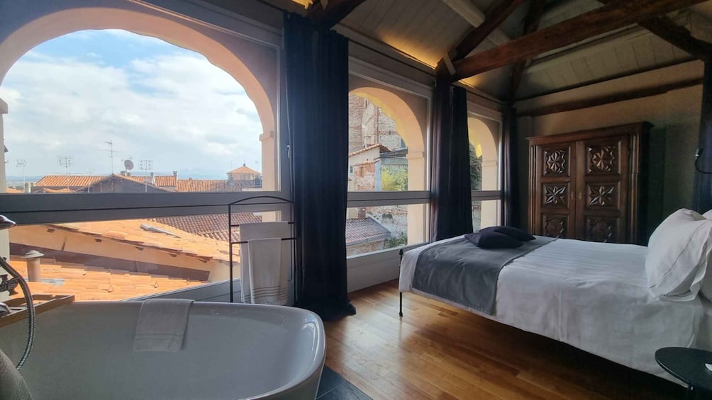 A bedroom with a large window, a bed, and a bathtub. 1