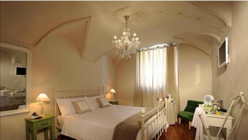 A bedroom with a large bed, a chandelier, a green chair, and a vanity with a mirror. 5