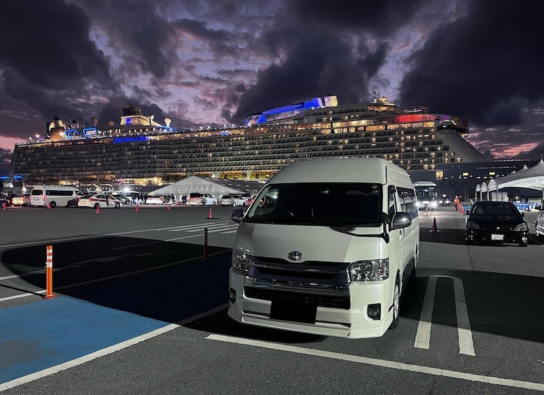 A white van parked in a port area with a large cruise ship in the background. 2