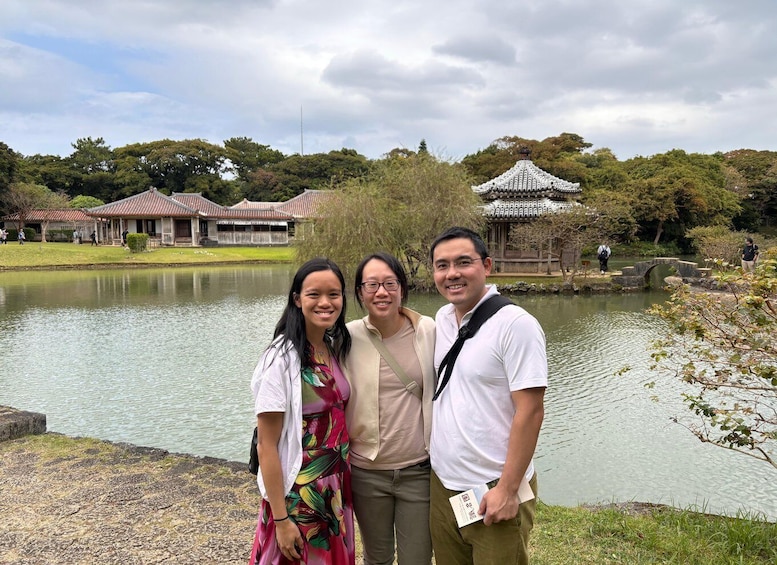 A group of people standing by a lake with traditional buildings and a pagoda in the background. 3