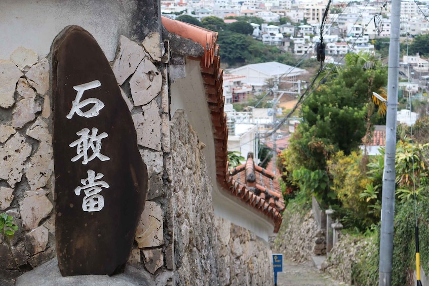 A stone wall with a sign, a tiled roof, and a view of a residential area. 4