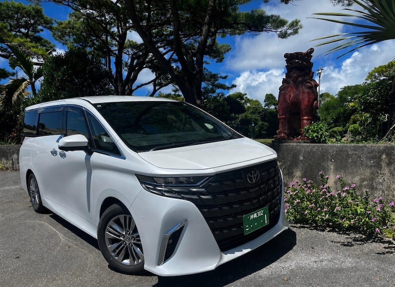 A white Toyota minivan parked in a parking lot with trees and a statue in the background. 5