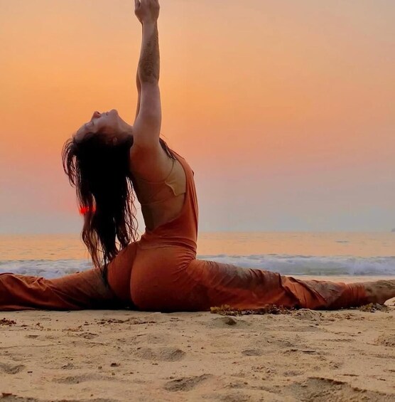 A person in a red dress performing a yoga pose on a beach at sunset. 3