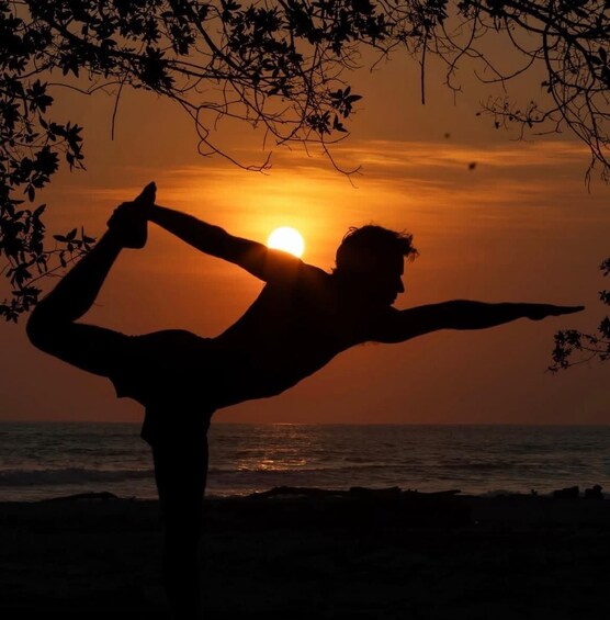 A silhouette of a person performing a yoga pose against a sunset at the beach. 1