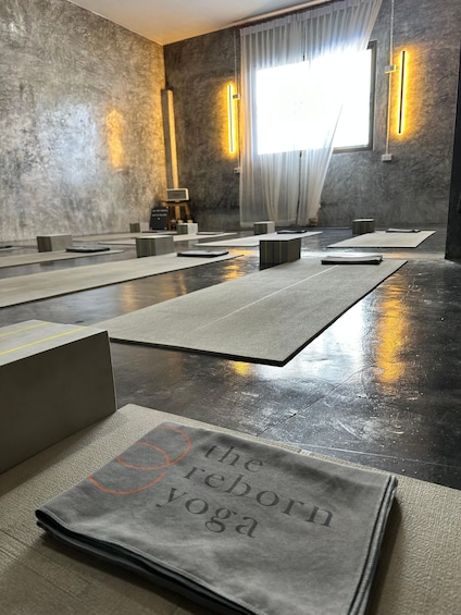 A yoga studio with mats and blocks on the floor, a wall-mounted light, and a window with curtains. 4