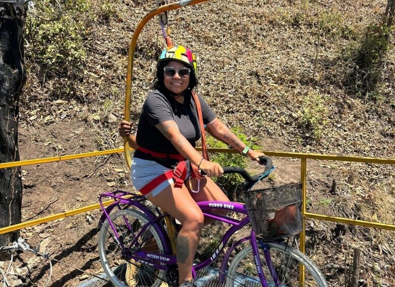 A person riding a purple bicycle with a basket, wearing a helmet and a black shirt, on a dirt path with yellow railings. 2