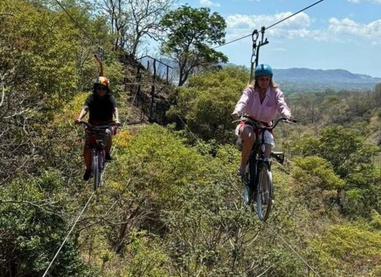 Two people riding bicycles on a suspension bridge surrounded by dense vegetation and hills. 2