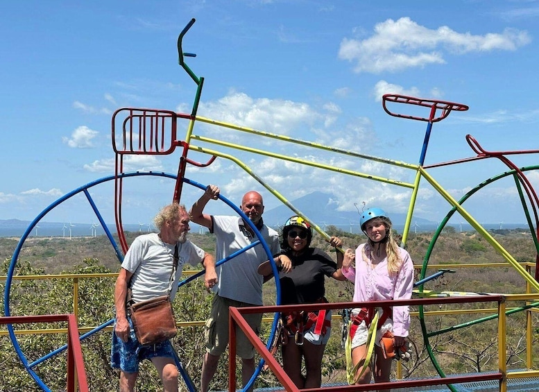 A group of people posing in front of a colorful bicycle structure with wind turbines in the background. 1