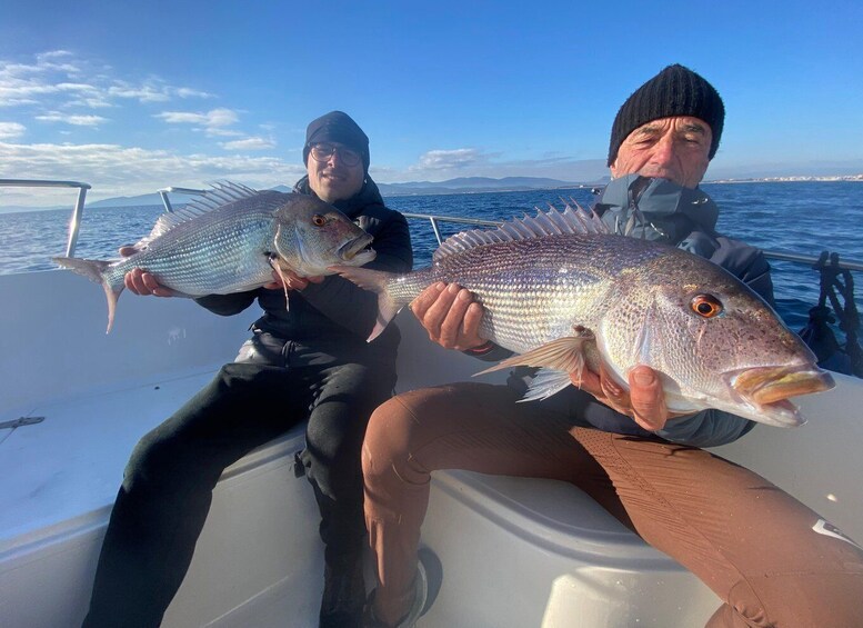 Two people on a boat holding large fish. 2