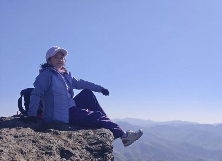 A person sitting on a rocky outcrop with a mountainous landscape in the background. 4