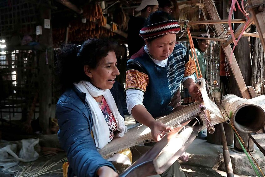 Two individuals engaged in weaving with a loom, surrounded by wooden structures and tools. 3