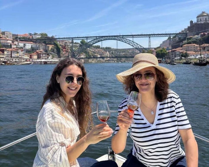 Two people toasting with wine glasses on a boat with a bridge and buildings in the background. 1