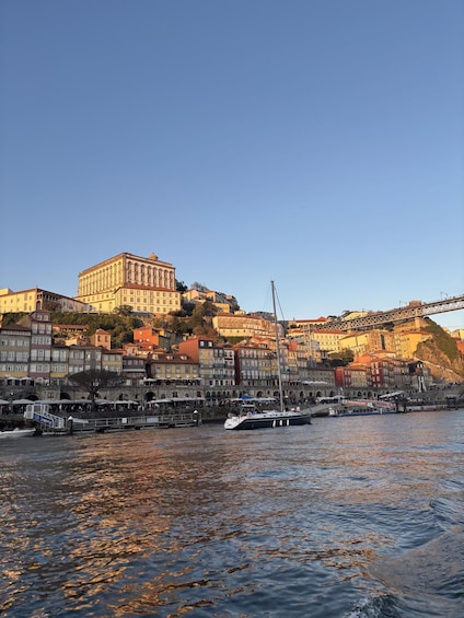 A waterfront cityscape with historic buildings, a prominent castle-like structure, and boats docked along the quay. 2