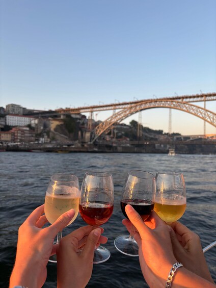 Four hands holding wine glasses with a bridge and buildings in the background. 3