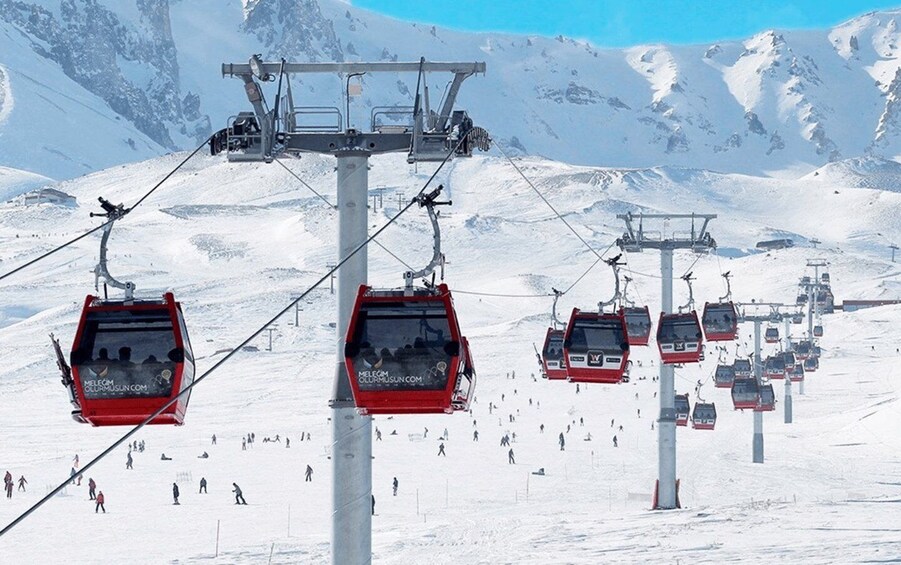 A ski lift with red gondolas carrying skiers against a snowy mountain backdrop. 1