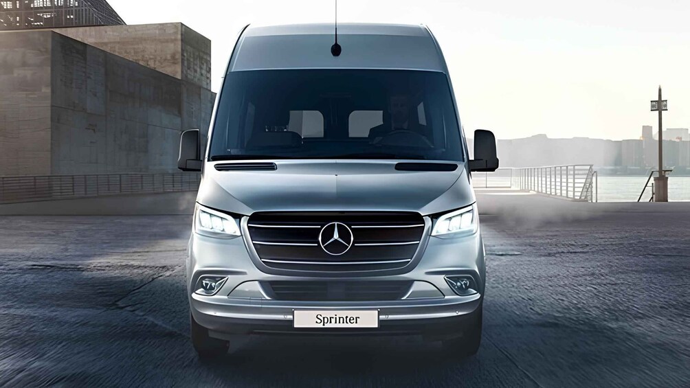 A silver Mercedes Sprinter van parked on a waterfront with a cityscape in the background. 3