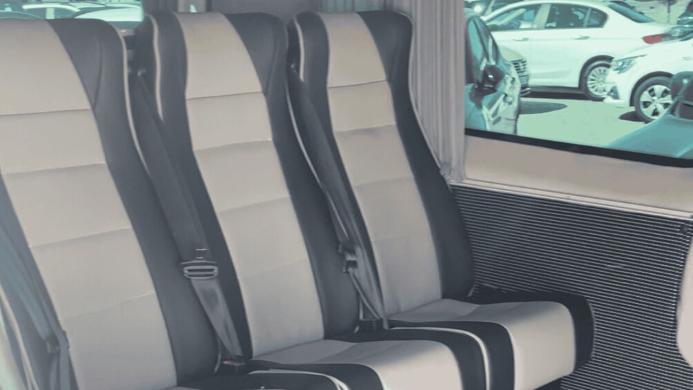 A vehicle interior with two seats, seat belts, and a window view of a parking lot with cars. 2