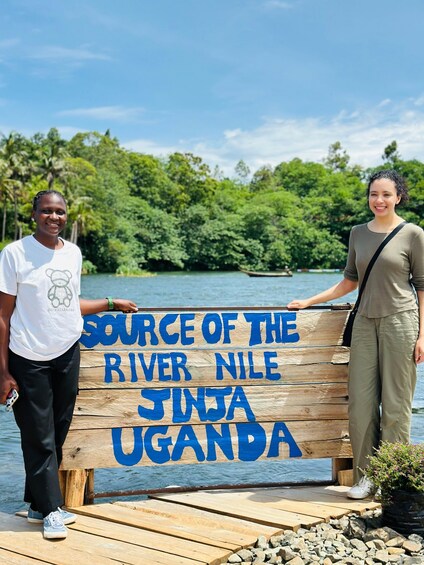 Two people standing by a wooden sign that reads 'Source of the River Nile, Jinja, Uganda.' 3