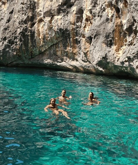 Three people swimming in clear turquoise water with rocky cliffs in the background. 3