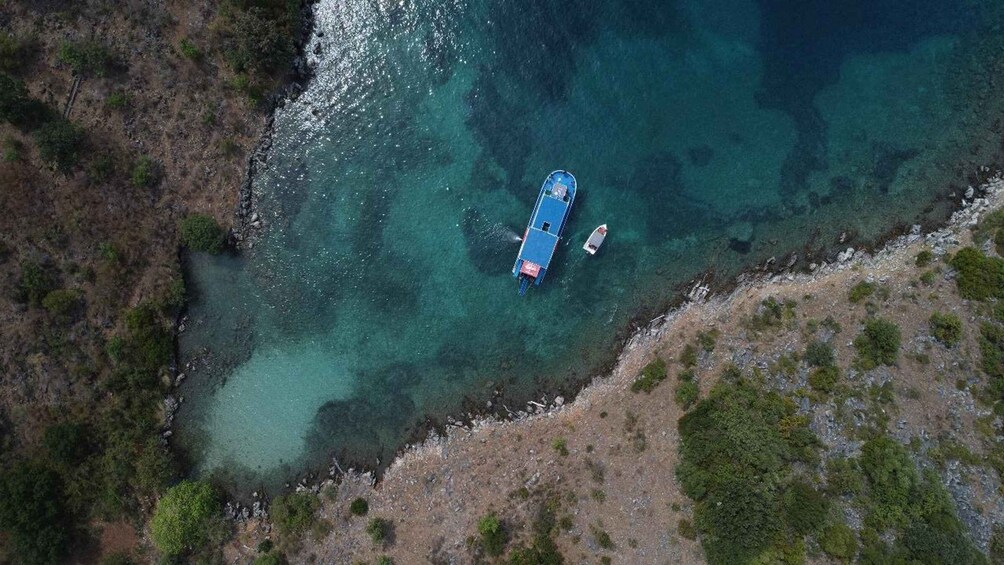 An aerial view of a coastal area with clear turquoise waters, a blue boat docked near the shore, and a rocky terrain with sparse vegetation. 5