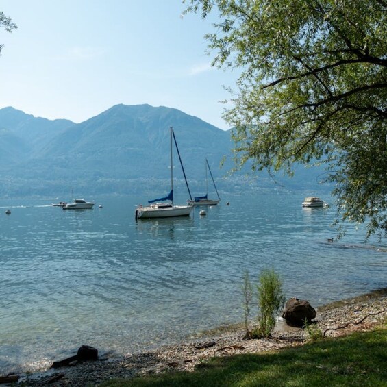 A calm lake with sailboats, a rocky shore, and mountains in the background. 3