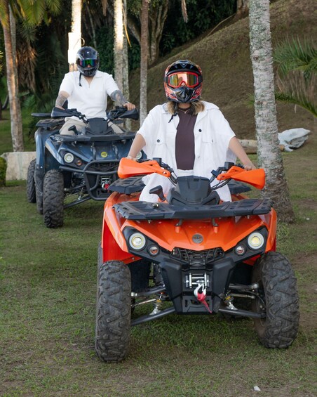 Two people on ATVs in a grassy area with trees. 3