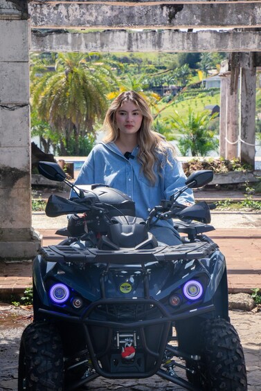 A person sitting on a black ATV with blue lights, parked in front of a concrete structure with palm trees in the background. 2