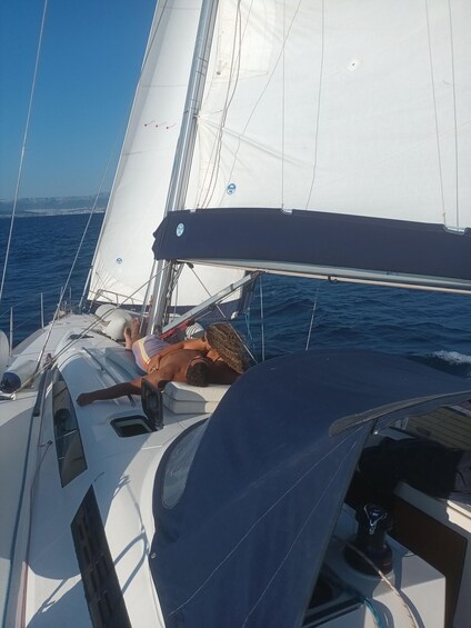 A sailboat with a person lying on the deck, a clear sky, and the sea in the background. 2
