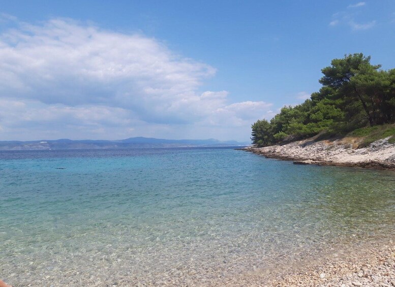 A clear coastal beach with pebbly shore, calm sea, and distant mountains. 4