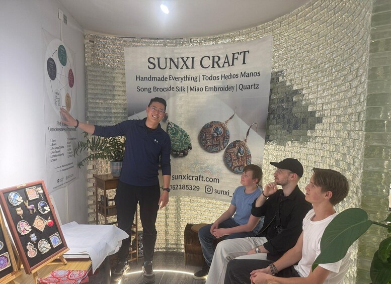 A person presenting in front of a wall with a banner for SUNXI CRAFT, featuring handmade items like silk and embroidery. 1