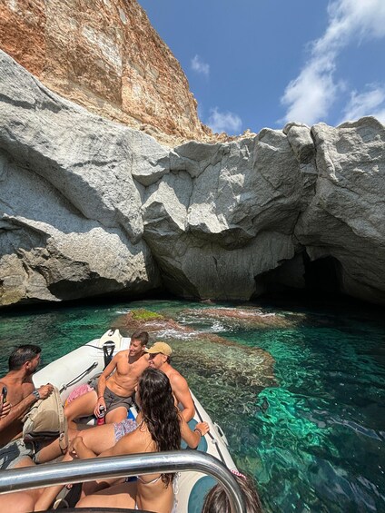 A group of people on a boat near rocky cliffs and clear water. 1
