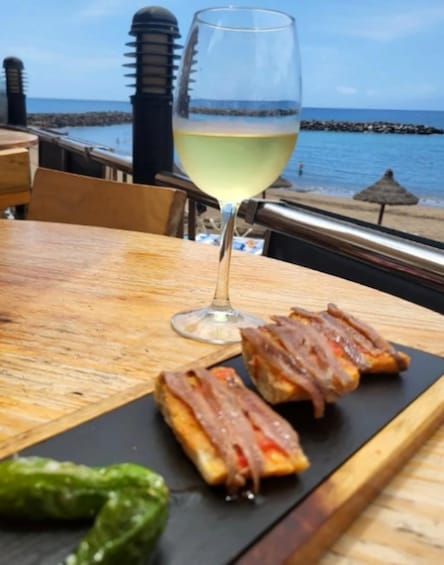 A table with a glass of white wine, two pastries, and a green chili pepper. 2