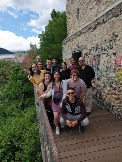 Un groupe de personnes se trouve sur un pont en bois, et on peut voir des graffitis sur le mur qui se trouve derrière elles. 1