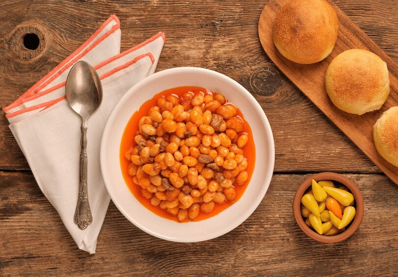 A bowl of beans with bread rolls on a wooden table. 5