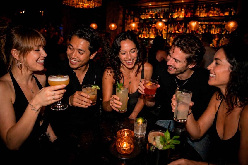 A group of people toasting with drinks at a bar with a dimly lit background and shelves of bottles. 1