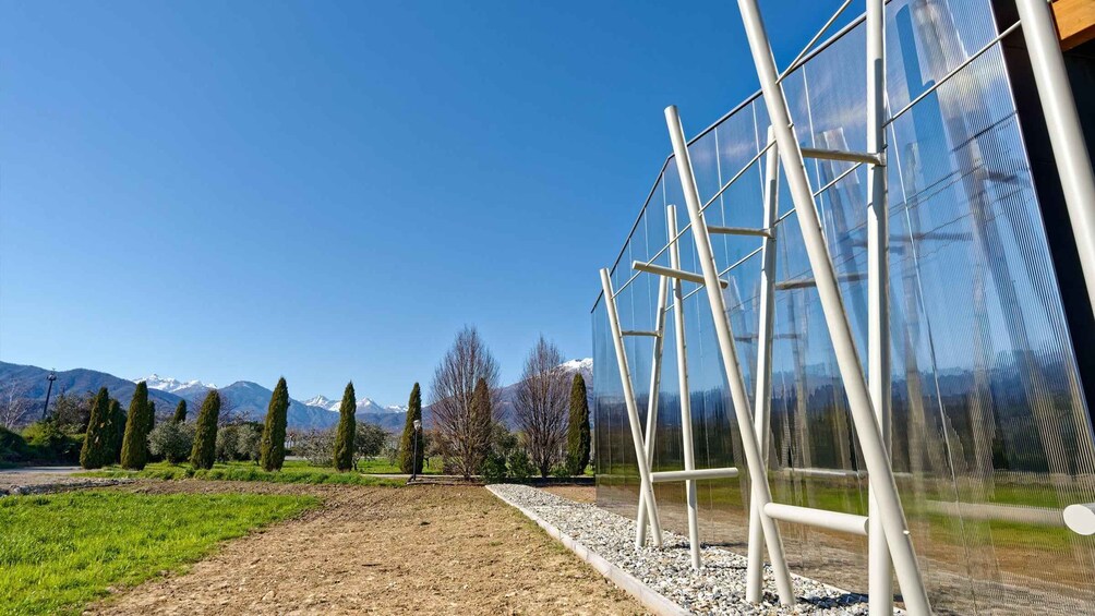 A clear sky, a dirt path, green grass, trees, and a mountain range in the distance. 1