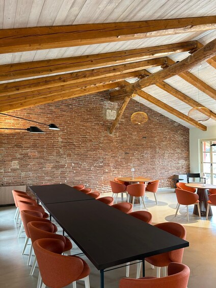 A spacious room with a long table, orange chairs, a brick wall, and wooden beams on the ceiling. 5
