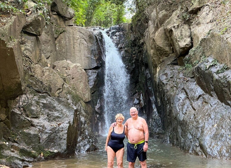 A waterfall in a rocky gorge with two people standing in the water. 4