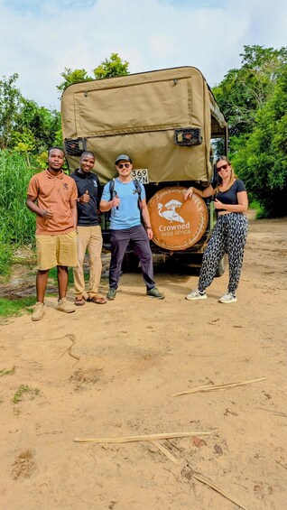 Four people standing in front of a safari vehicle with a logo and a license plate. 4