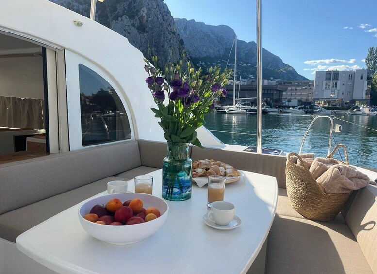 A boat deck with a table set for breakfast, including a bowl of fruit, a vase with flowers, and a basket of bread. 5