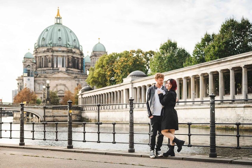A couple standing on a bridge with a historic building in the background. 1