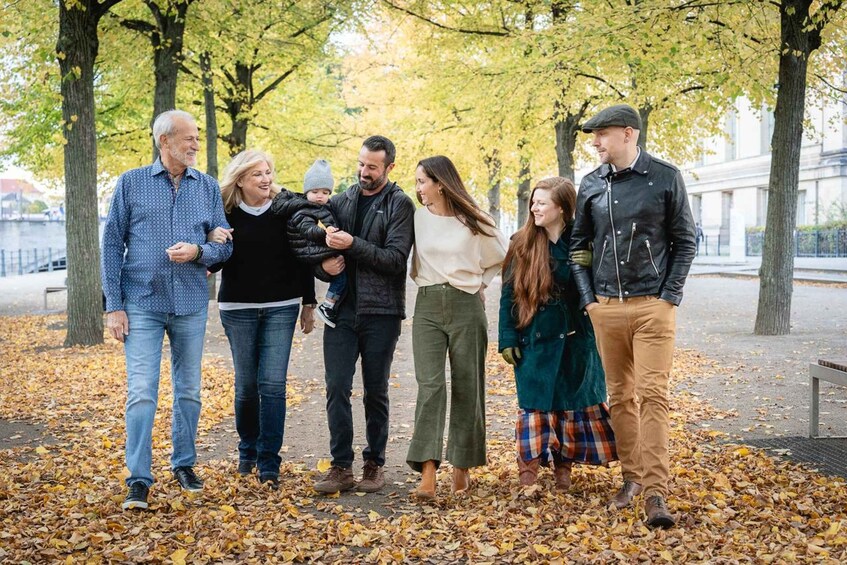 A group of people walking on a leaf-covered path in a park with trees and a building in the background. 3