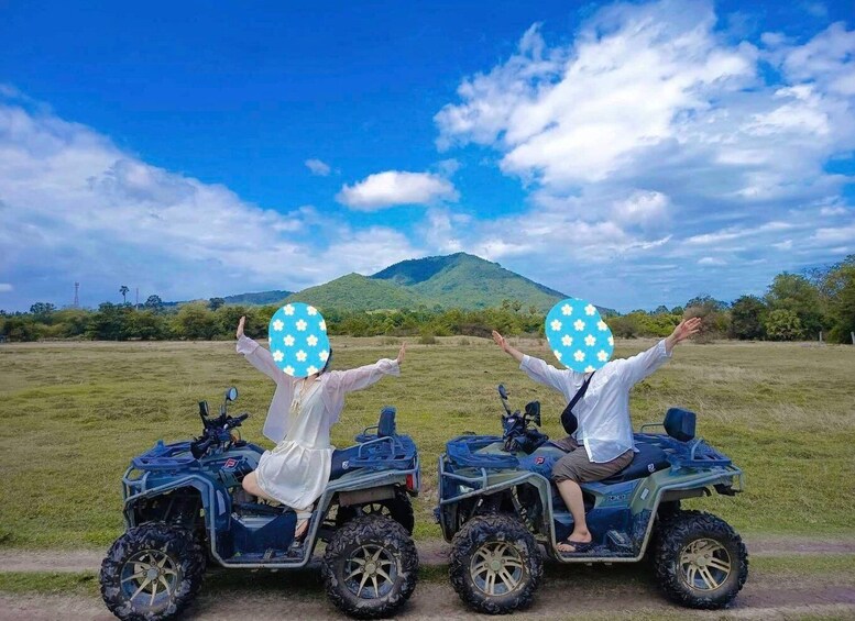 Two people on ATVs with flower-patterned helmets, a grassy field, and a mountain in the background. 4