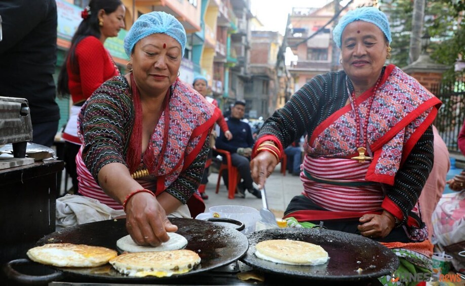 Two women cooking flatbreads on a street. 1