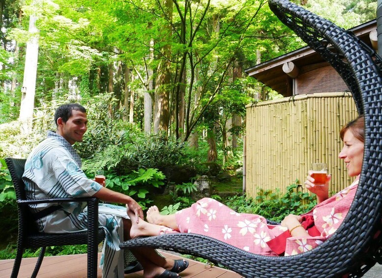 Two people sitting on wicker chairs in a garden with bamboo fencing and lush greenery. 3