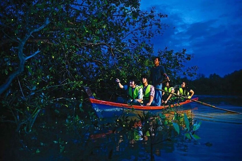 A group of people in a boat on a calm body of water at night, surrounded by dense foliage. 4