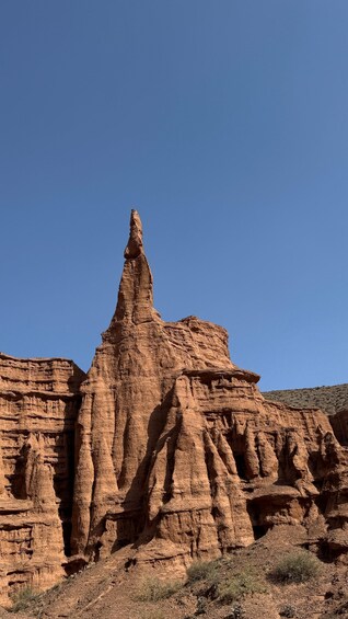 A prominent rock formation with a narrow peak, surrounded by layered sedimentary cliffs. 1