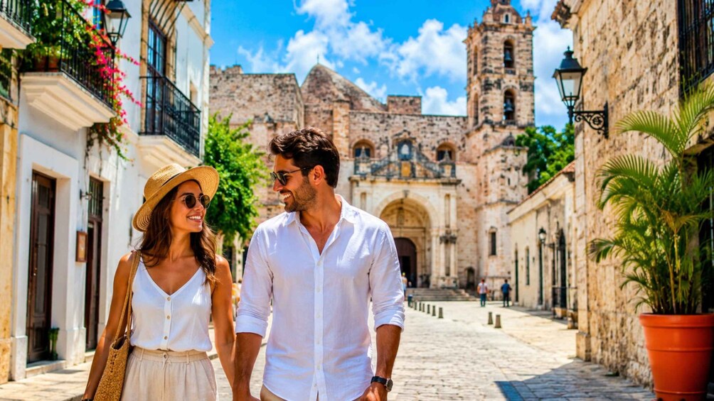A couple walking down a cobblestone street with historic buildings and a church tower in the background. 1